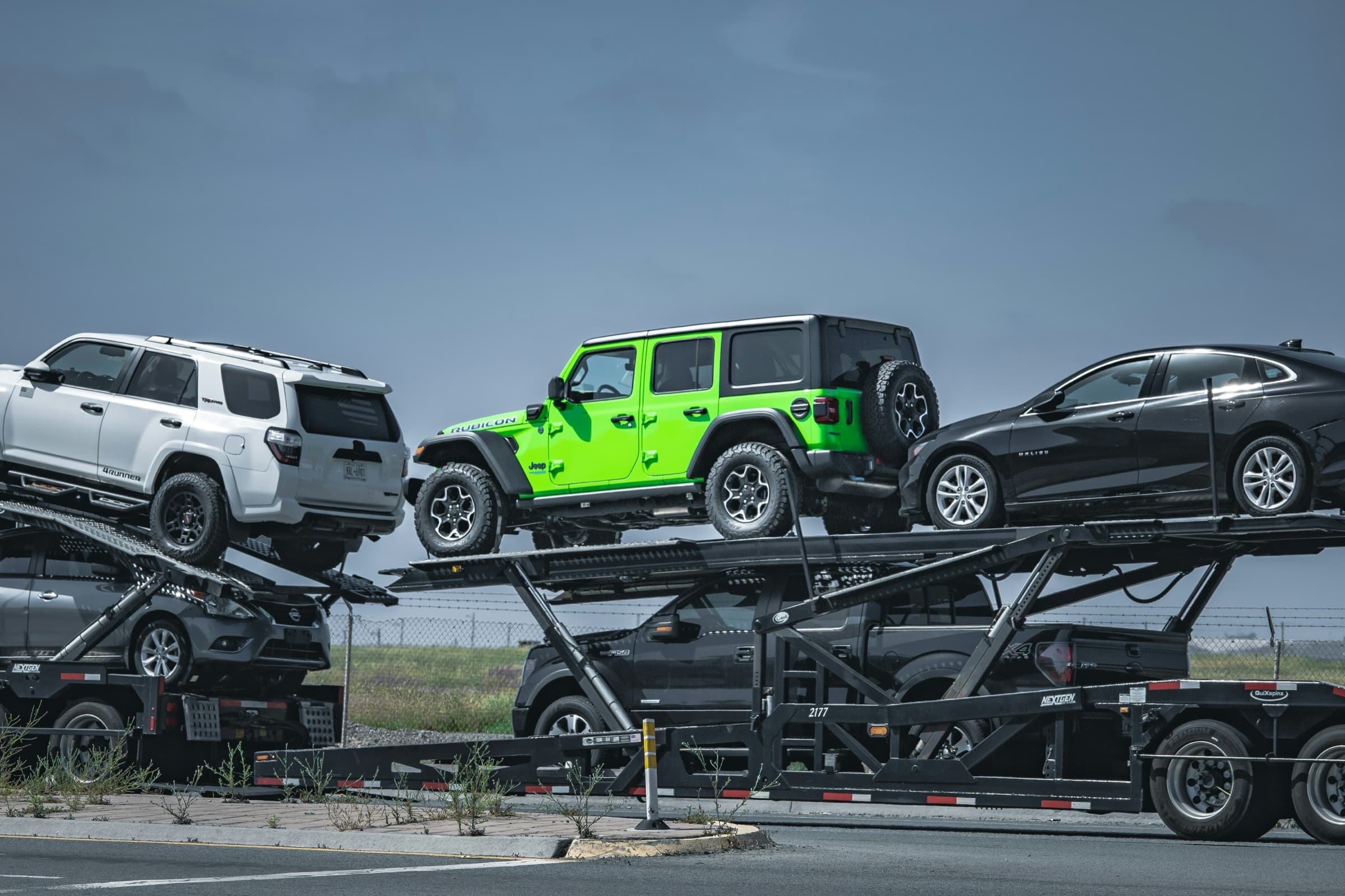 An open auto-transport carrier loaded with SUVs, a Jeep, and sedans
